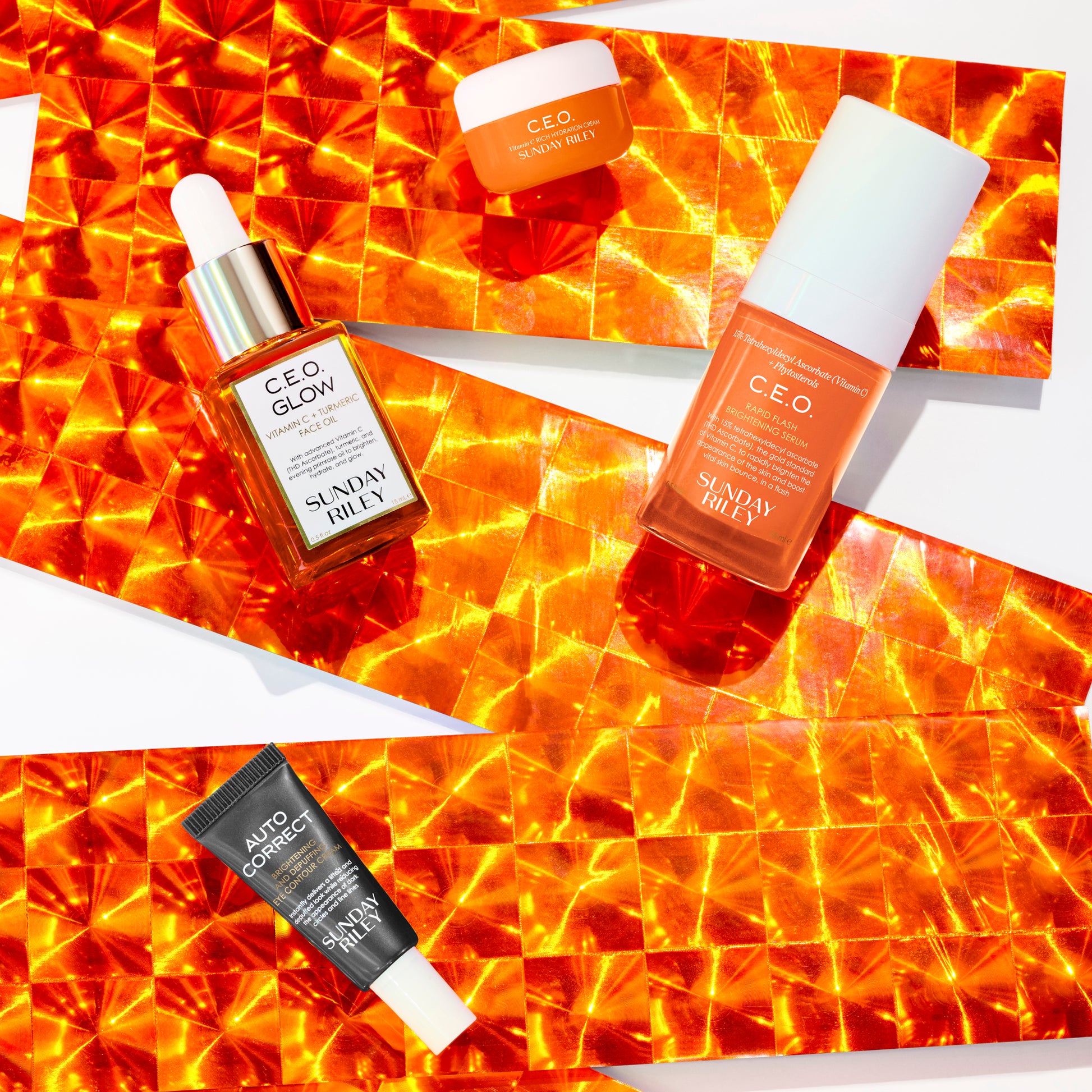 C.E.O. Glow, C.E.O. Serum, Auto Correct and C.E.O. Cream bottles over a orange reflective ribbon on white background