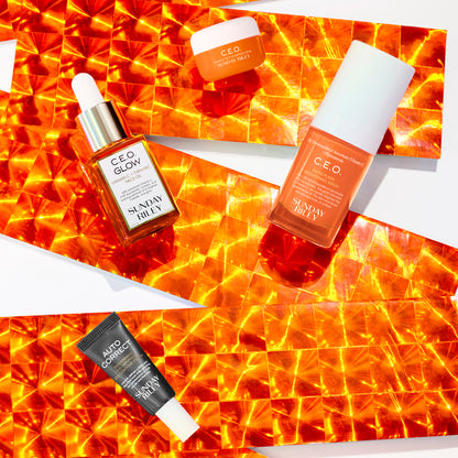 C.E.O. Glow, C.E.O. Serum, Auto Correct and C.E.O. Cream bottles over a orange reflective ribbon on white background