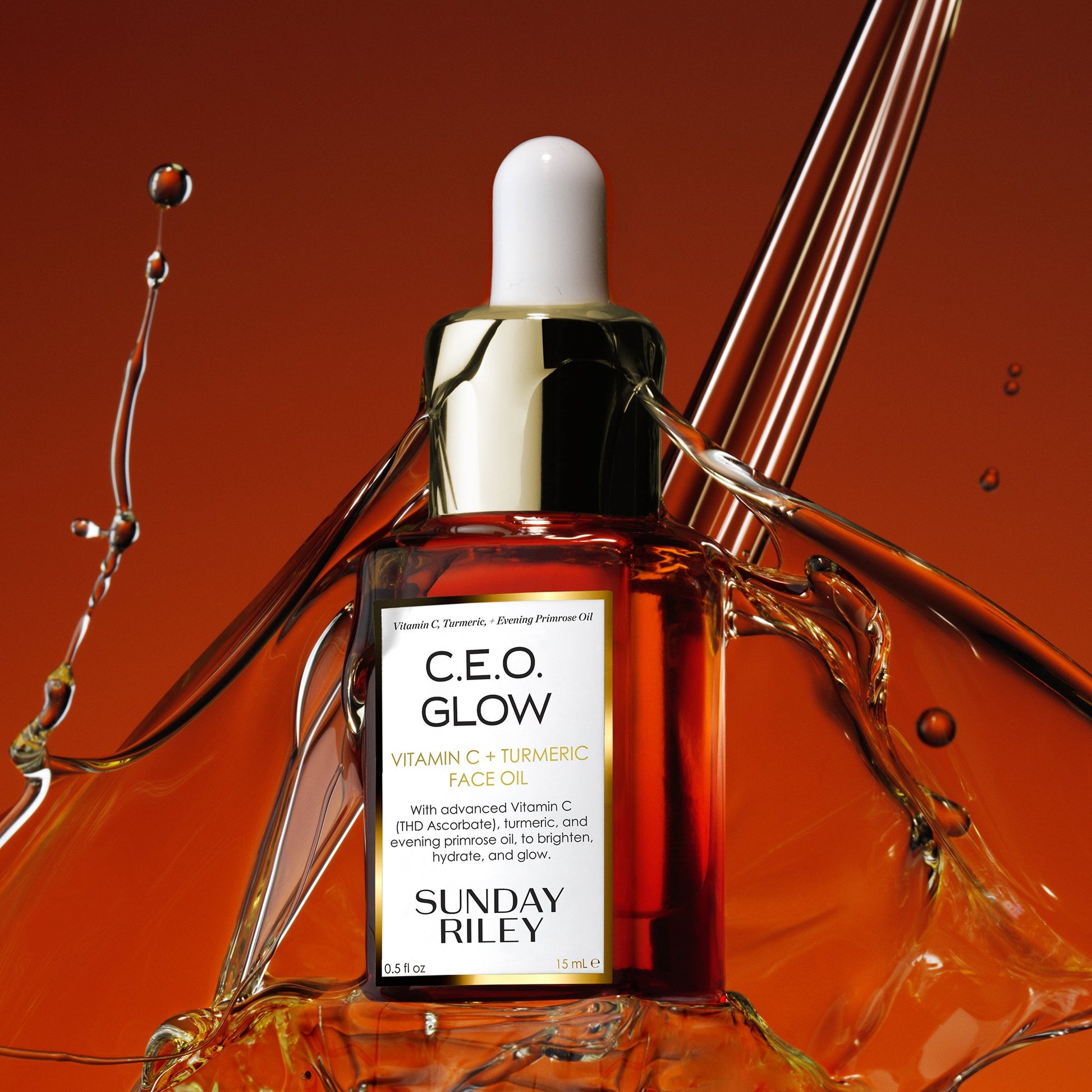 C.E.O. Glow Face Oil in a orange gradient glass bottle with silicon dropper with splashes of oil in the background.