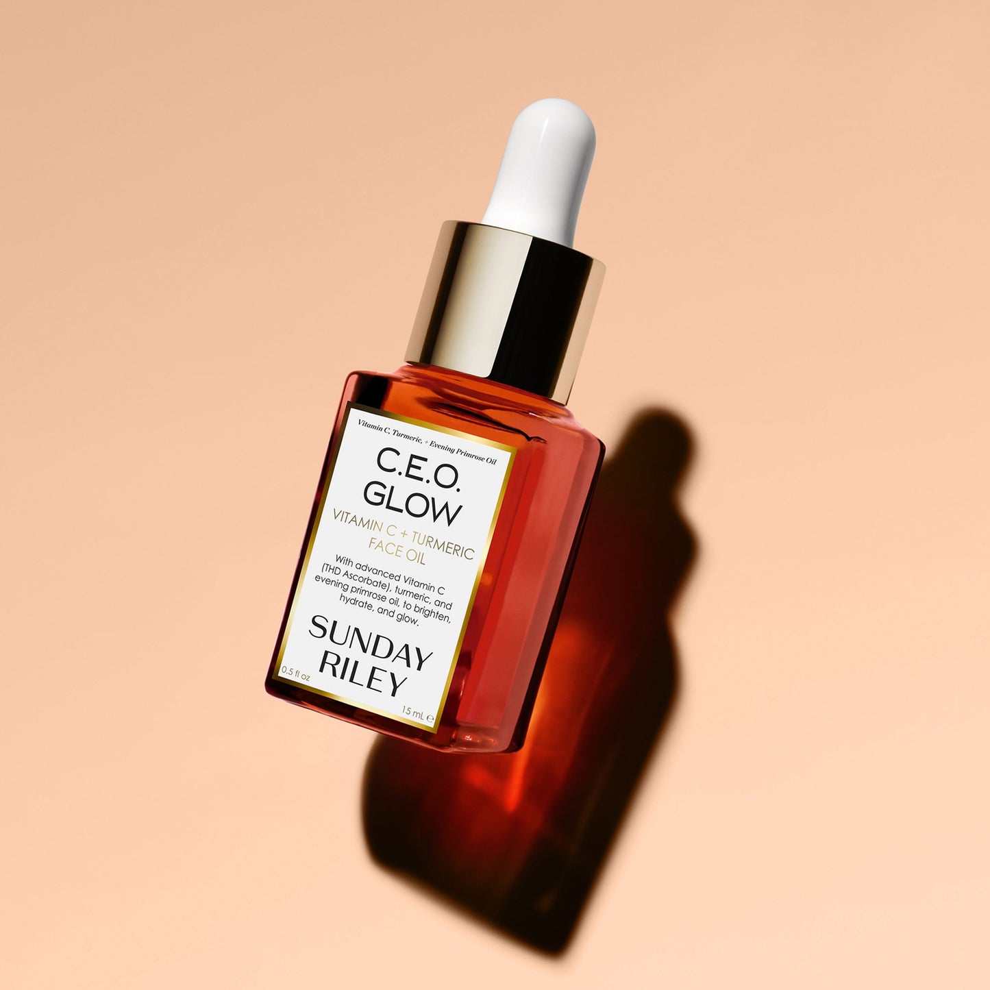 Lay down of C.E.O. Glow Face Oil bottle with shadow on a peach background