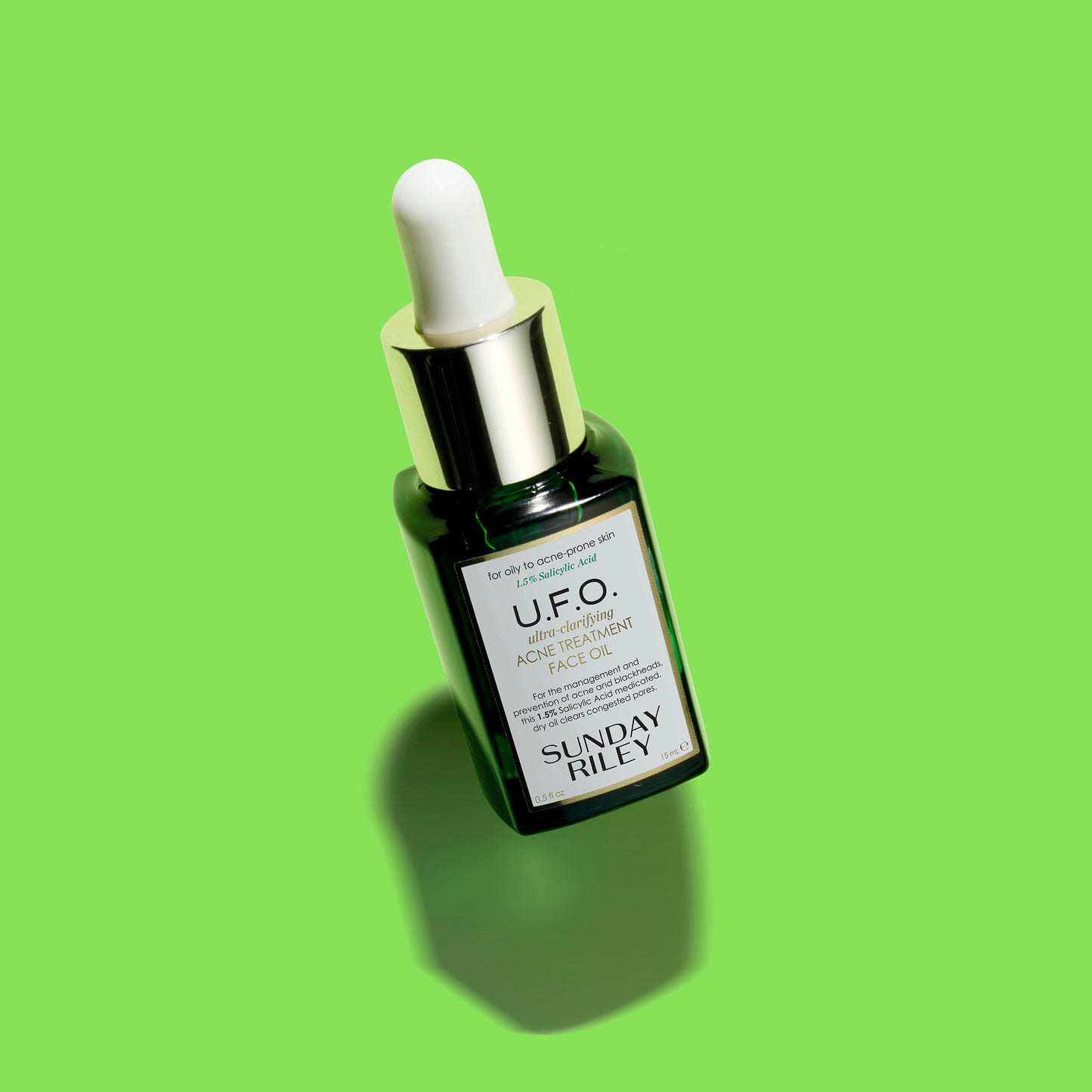 A tilted U.F.O. Acne Treatment Face Oil in a green gradient glass bottle with silicon dropper with a lime green background.