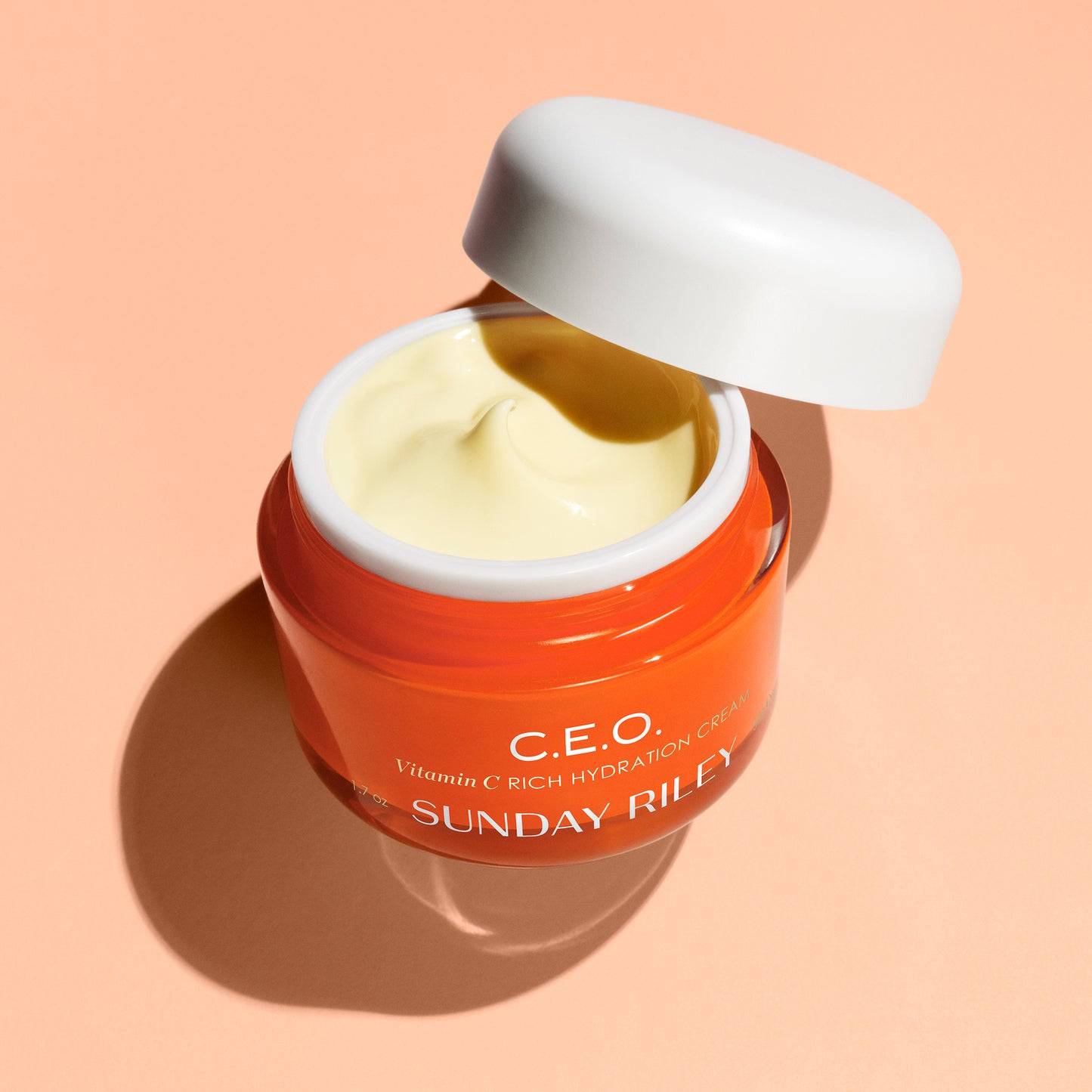 Pastel orange background, open CEO moisturizer jar, light yellow moisturizer cream 